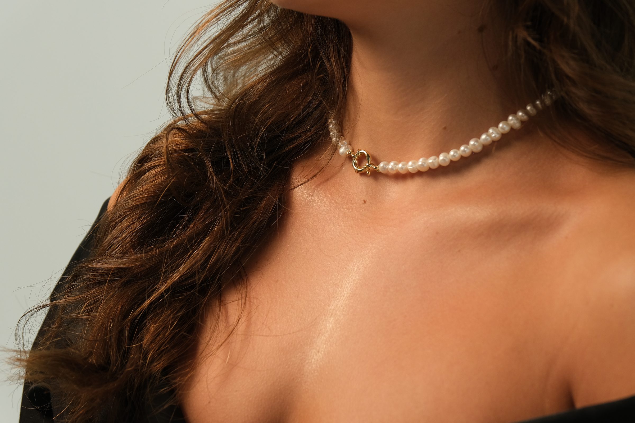 Parelchoker met gouden sluiting rond de hals, elke parel net anders van vorm